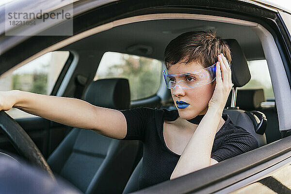Frau mit blauem Lippenstift und intelligenter Brille fährt Auto