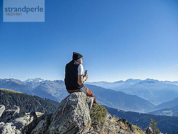 Älterer Mann mit Wasserflasche sitzt an einem sonnigen Tag auf einem Felsen im Nationalpark Vanoise  Frankreich