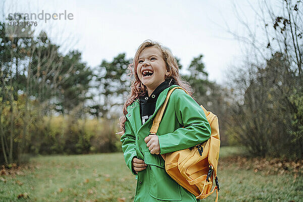 Fröhliches Mädchen mit gelbem Rucksack steht im Park