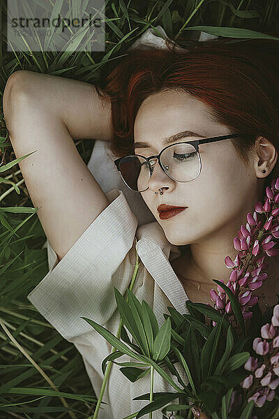 Redhead girl lying on grass with lupin flowers