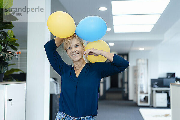 Glückliche Geschäftsfrau mit Luftballons im Büro