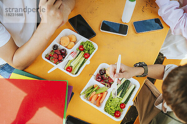 Schüler sitzen mit Smartphones am Tisch und essen zu Mittag
