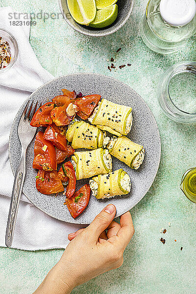 Persönliche Perspektive einer Frau  die einen Teller mit Zucchini- und Ricotta-Brötchen mit Tomatensalat in die Hand nimmt