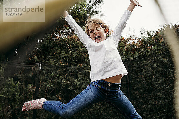 Playful girl with arms raised jumping in garden
