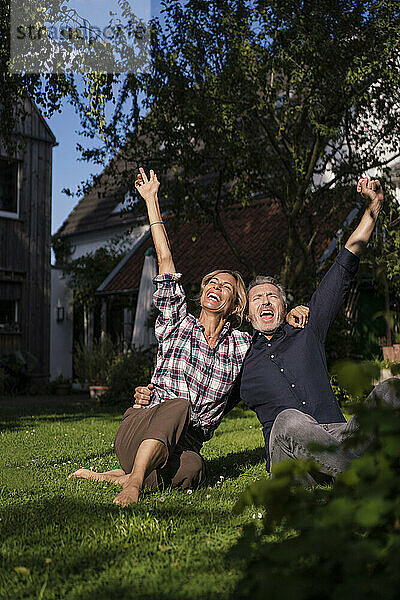 Fröhlicher Mann und Frau mit erhobenen Armen genießen es im Hinterhof