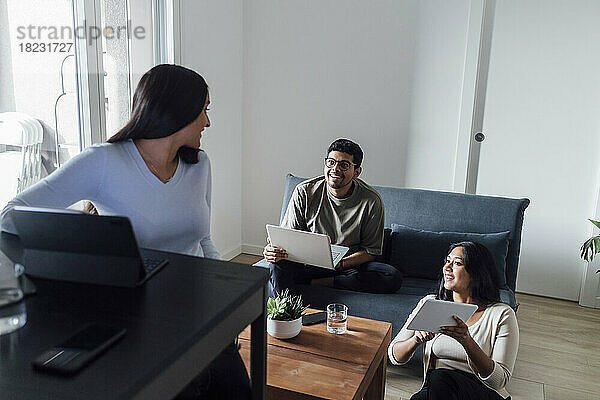 Smiling man and women with wireless technologies discussing at home