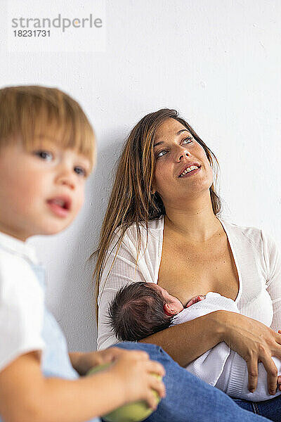 Nachdenkliche Mutter stillt neugeborene Tochter von Sohn zu Hause