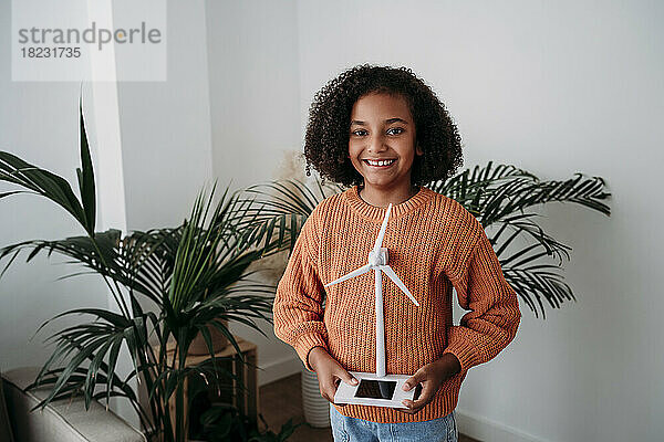 Glückliches Mädchen  das zu Hause mit dem Modell einer Windkraftanlage steht