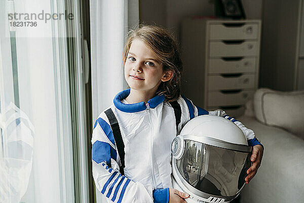 Mädchen im Weltraumkostüm mit Helm steht zu Hause am Fenster
