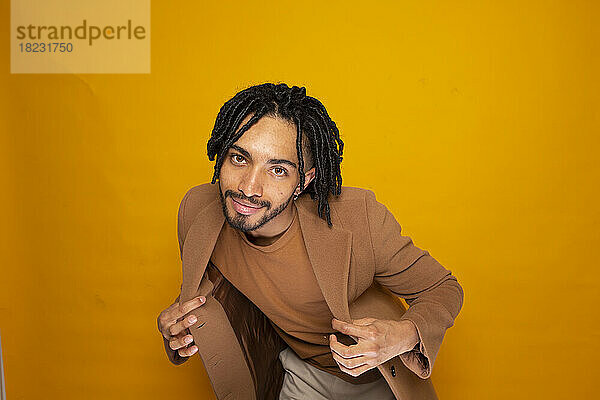 Smiling man with dreads posing against yellow background