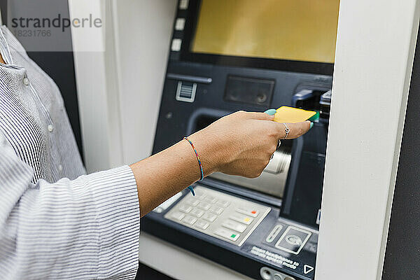 Hand einer Frau  die Kreditkarte in einen Geldautomaten einführt