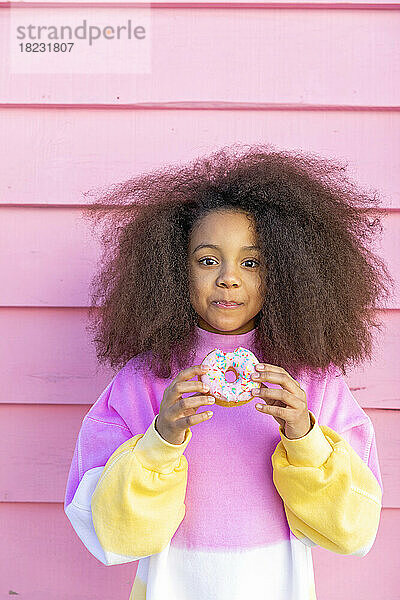 Afro-Mädchen mit Donut vor rosa Wand