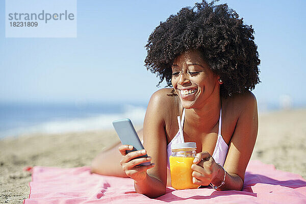 Glückliche Frau  die an einem sonnigen Tag ihr Smartphone am Strand benutzt