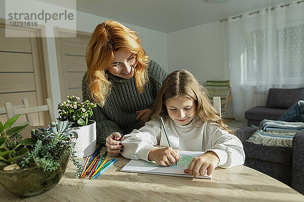 Mädchen zeichnet am Tisch ein Bild  beobachtet von ihrer Mutter