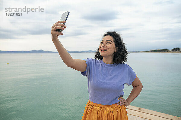 Lächelnde Frau  die ein Selfie vor dem Meer macht