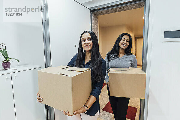 Smiling women holding boxes at door