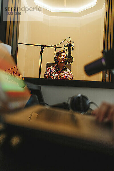 Happy singer recording music through microphone in studio