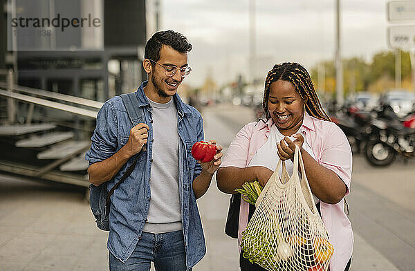 Glücklicher junger Mann und Frau halten eine Tüte Gemüse am Fußweg