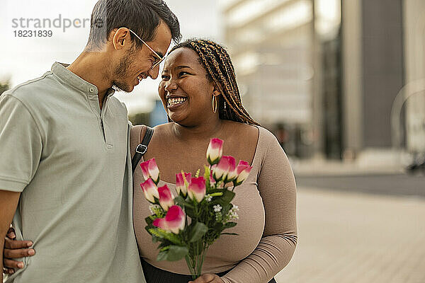 Happy young man embracing woman standing with bouquet of flowers
