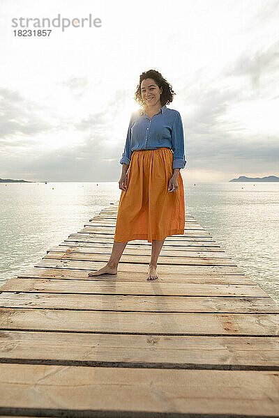 Lächelnde Frau steht auf einem Steg inmitten des Meeres