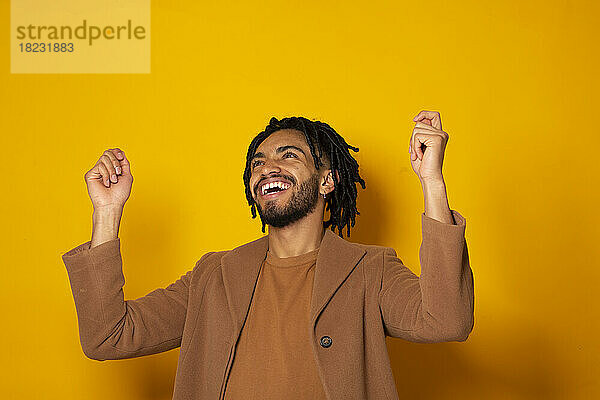 Young man cheering against yellow background