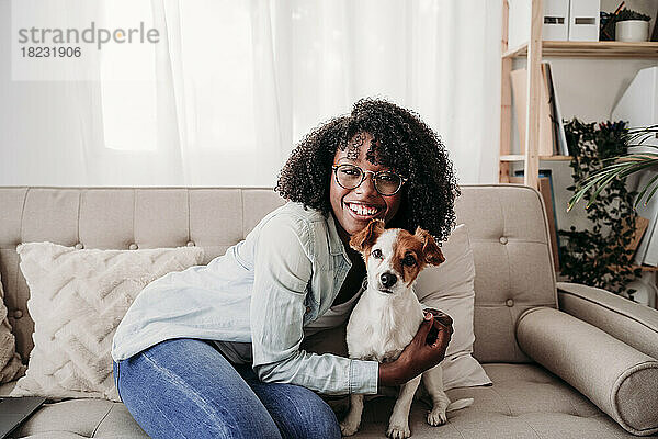 Glückliche Frau umarmt Hund  der zu Hause auf dem Sofa sitzt