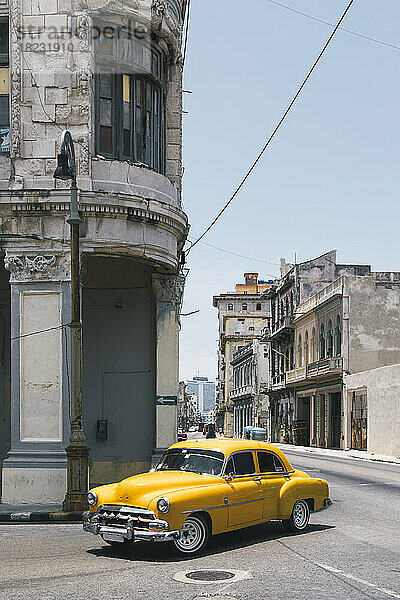 Kuba  Havanna  gelber Oldtimer fährt entlang der Straße im Centro Habana