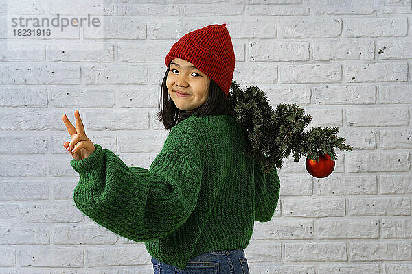 Smiling girl with Christmas tree gesturing peace sign