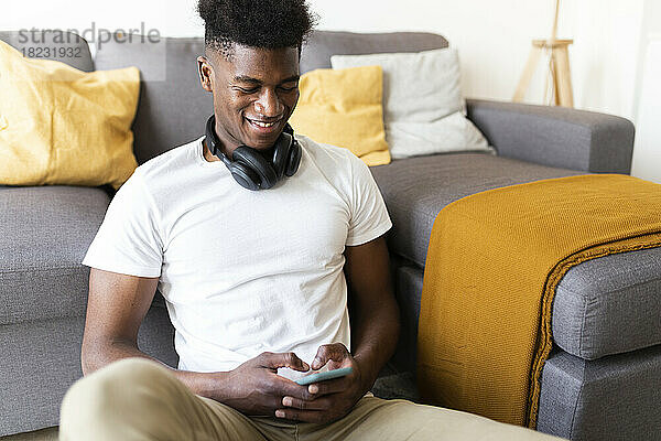Lächelnder Mann  der zu Hause auf dem Sofa sitzt und sein Mobiltelefon benutzt