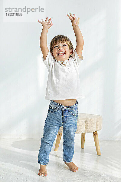 Boy with arms raised standing in front of wall at home