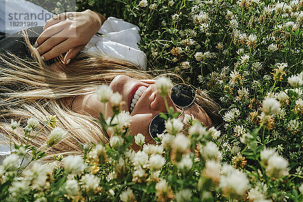 Glückliche Frau liegt auf einer unbewirtschafteten Wiese mit Wildblumen