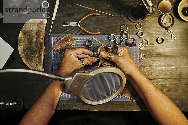 Hands of craftswoman polishing golden ring with sand paper on workbench