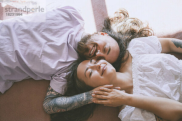 Happy romantic couple with eyes closed lying on bed at home