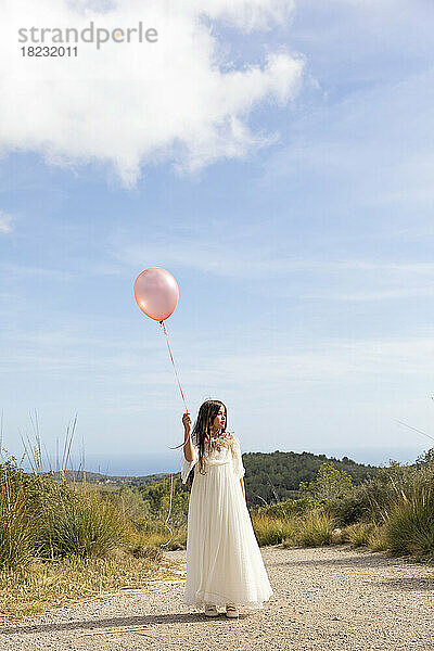 Mädchen im weißen Kleid mit rosa Luftballon läuft auf dem Weg