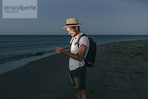 Lächelnder Mann  der nachts am Strand sein Smartphone benutzt