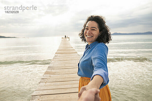 Fröhliche Frau hält die Hand eines Mannes auf einem Steg mitten im Meer