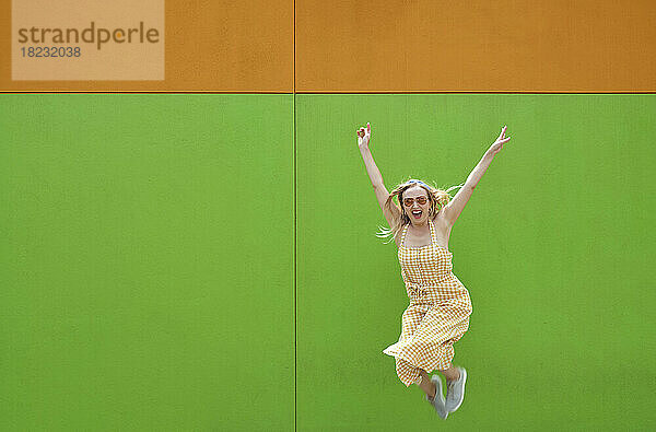 Fröhliche Frau springt vor grüne Wand
