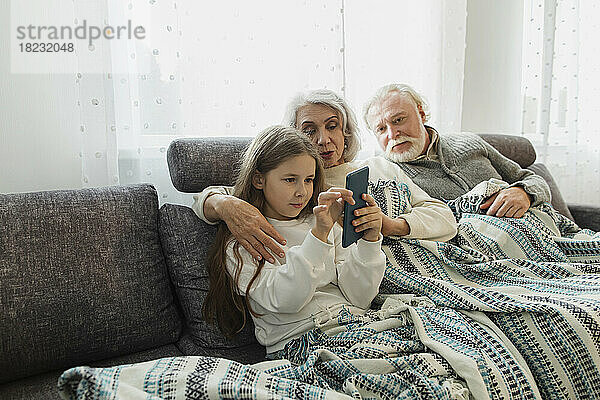 Grandparents and granddaughter sitting on couch under a blanket