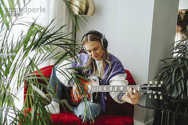 Gitarrist trägt Kopfhörer und spielt Gitarre auf einem Sessel im Studio