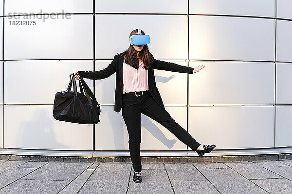 Junge Frau trägt einen Virtual-Reality-Simulator und hält eine Tasche vor der Wand