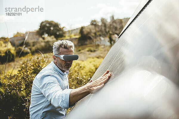 Reifer Mann mit VR-Brille berührt Solarpanel im Garten