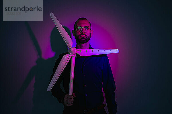 Pink light falling on businessman holding model of wind turbine in darkroom