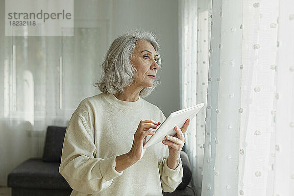 Ältere Frau hält digitales Tablet zu Hause