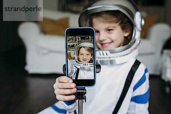 Lächelndes Mädchen im Weltraumkostüm  das zu Hause ein Selfie mit dem Handy macht