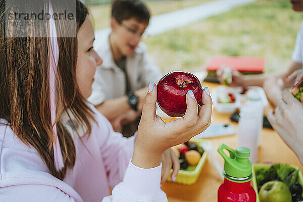 Mädchen hält Apfel während des Mittagessens auf dem Schulhof