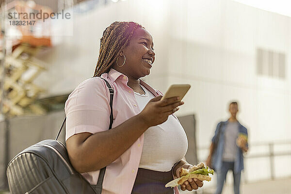 Lächelnde  kurvige Frau mit Smartphone und Sandwich
