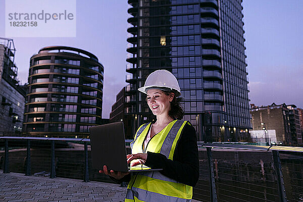 Glücklicher Ingenieur mit Laptop vor dem Gebäude in der Abenddämmerung