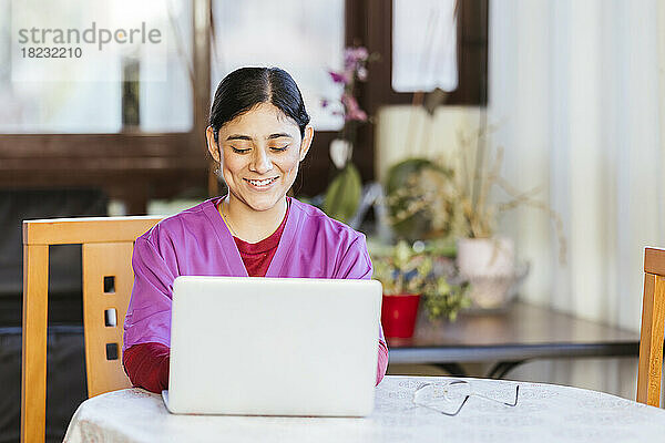 Lächelnder Mitarbeiter im Gesundheitswesen  der zu Hause einen Laptop benutzt