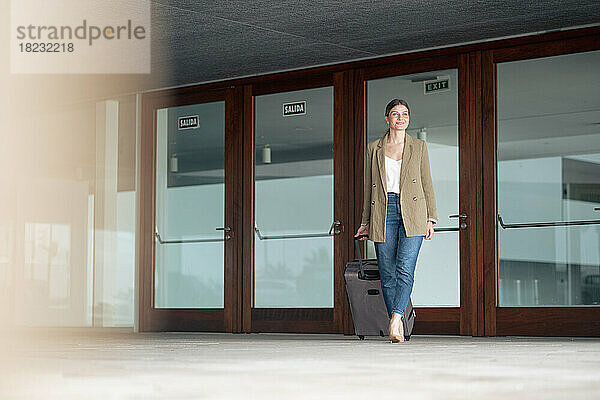 Lächelnde Geschäftsfrau  die mit Gepäck vor der Tür läuft