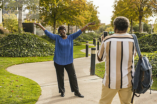 Mann fotografiert Frau  die mit erhobenen Armen im Park steht